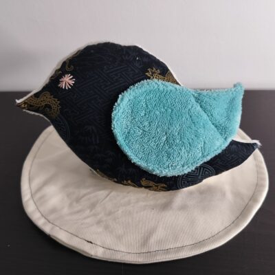 Peluche oiseau style japonais en tissu noir et doré avec une aile en éponge bleue et un œil étoile rose brodé main.