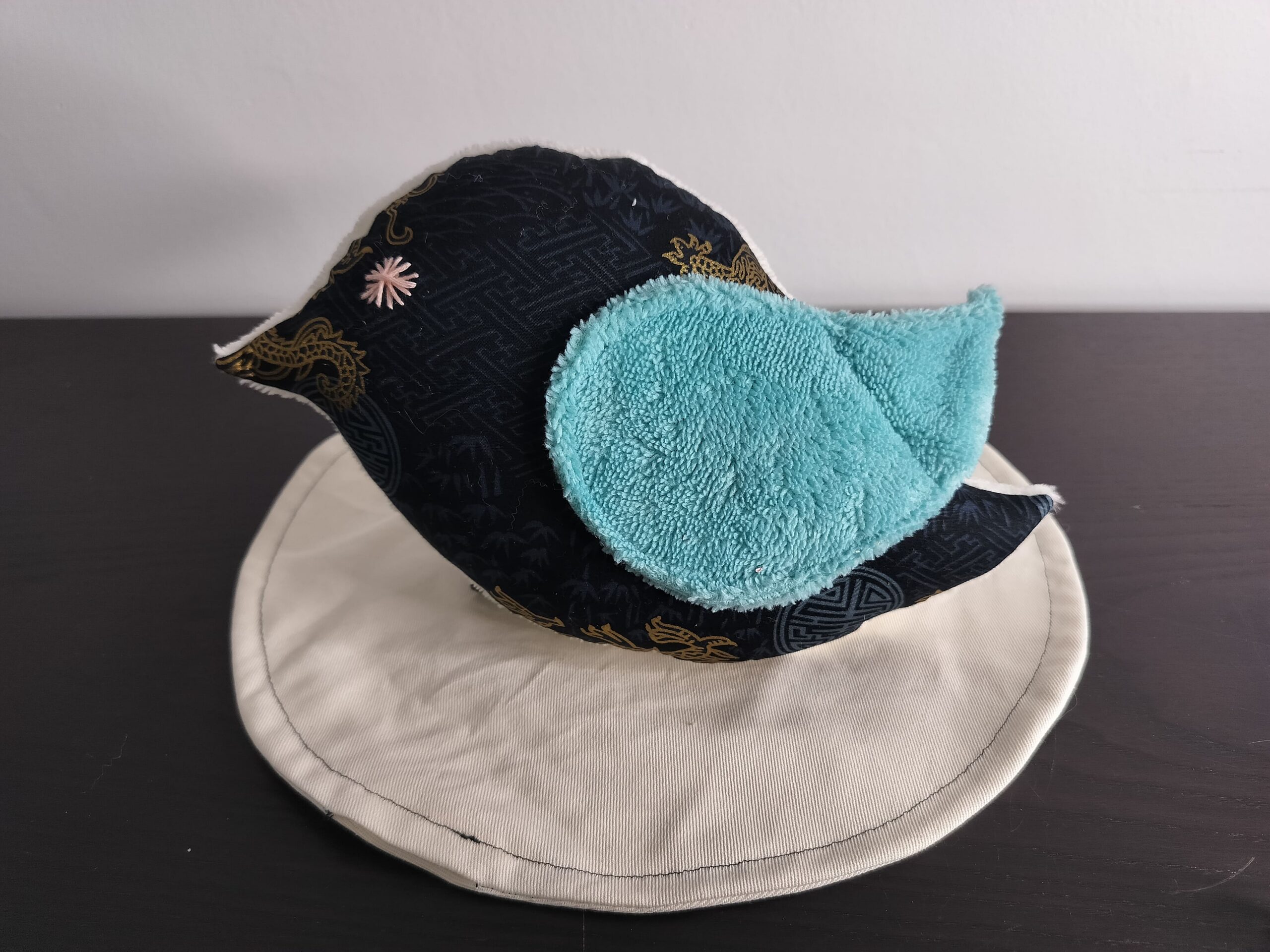 Peluche oiseau style japonais en tissu noir et doré avec une aile en éponge bleue et un œil étoile rose brodé main.