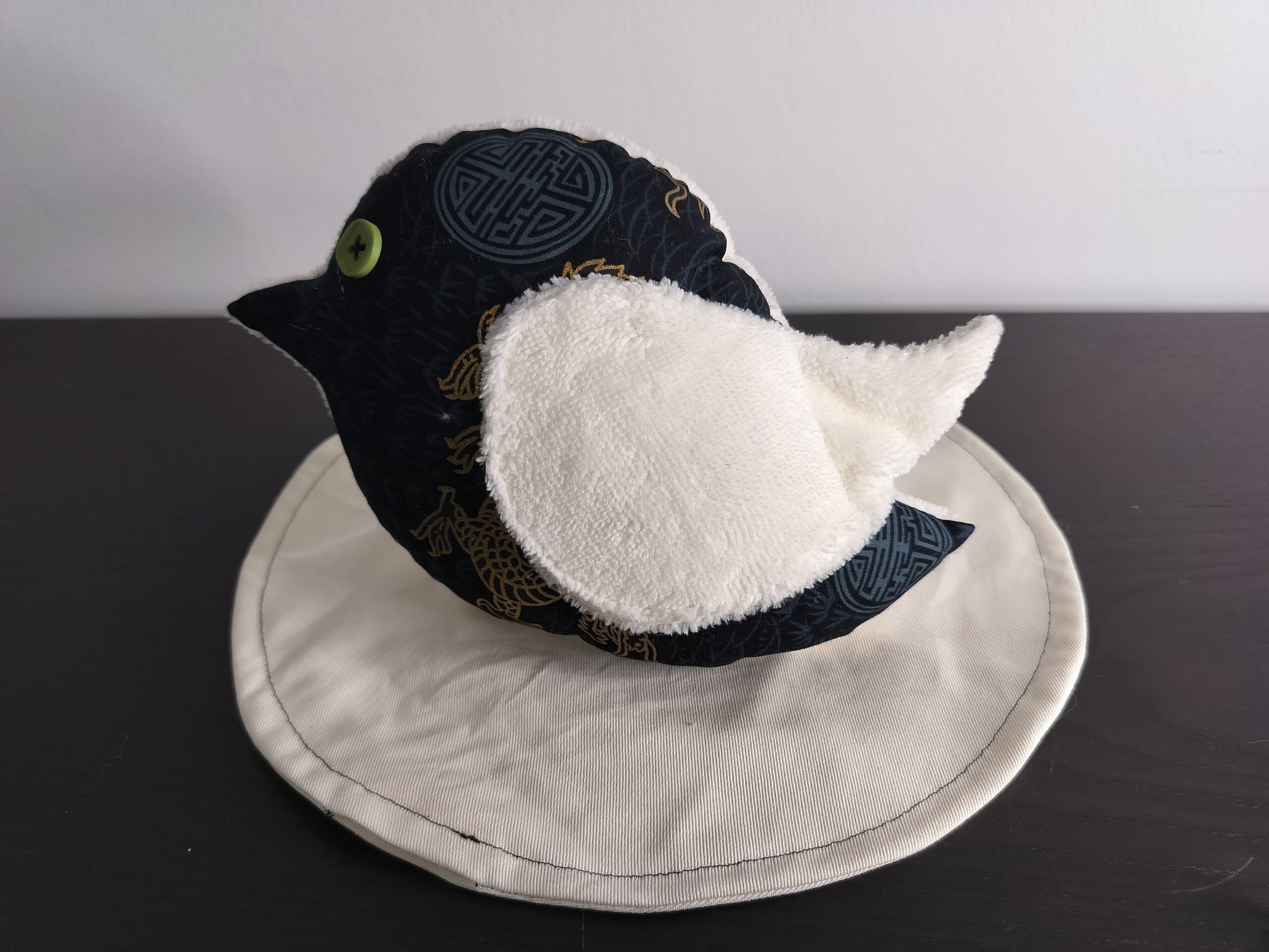 Peluche oiseau style japonais en tissu noir et doré avec une aile en éponge blanche et un œil bouton vert.