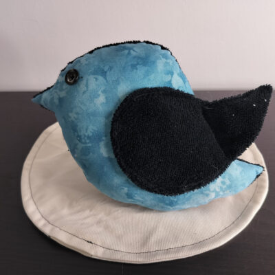 Peluche oiseau bleu en tissu marbré avec une aile en éponge noire et un œil bouton noir classique.