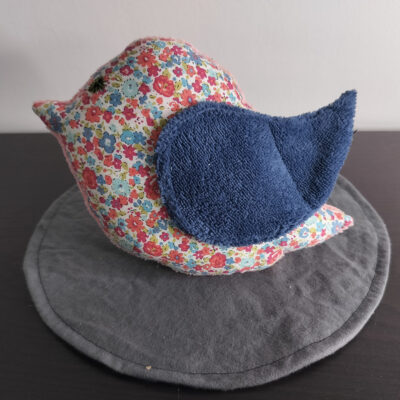 Peluche oiseau liberty en tissu fleuri avec une aile en éponge bleue et un œil bouton noir.
