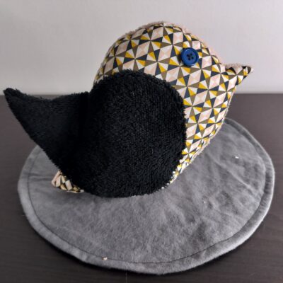 Peluche oiseau à motifs géométriques avec une aile en éponge noire et un œil bouton bleu.