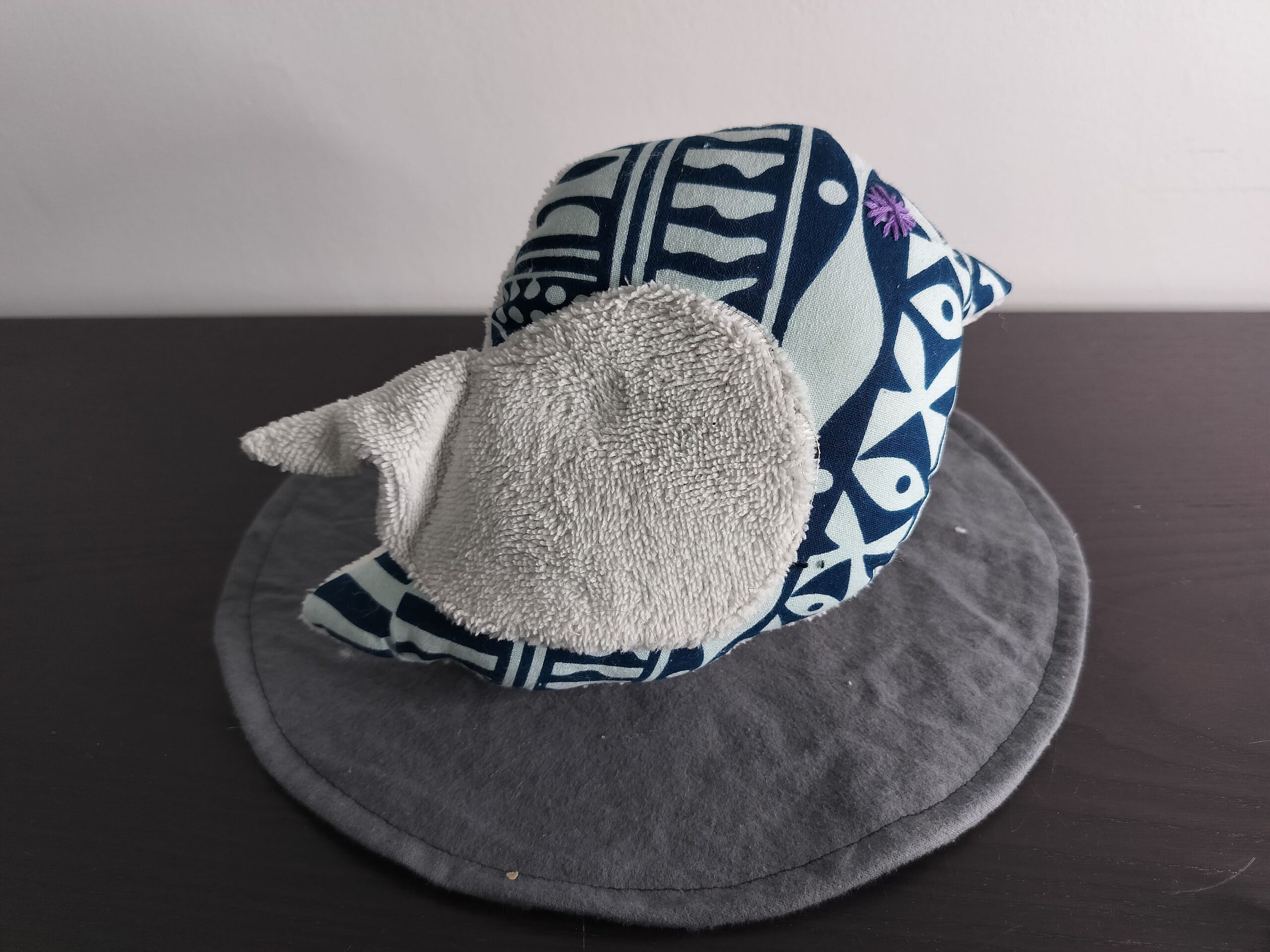 Oiseau décoratif en tissu wax bleu avec une aile en éponge gris clair et une broderie violette.