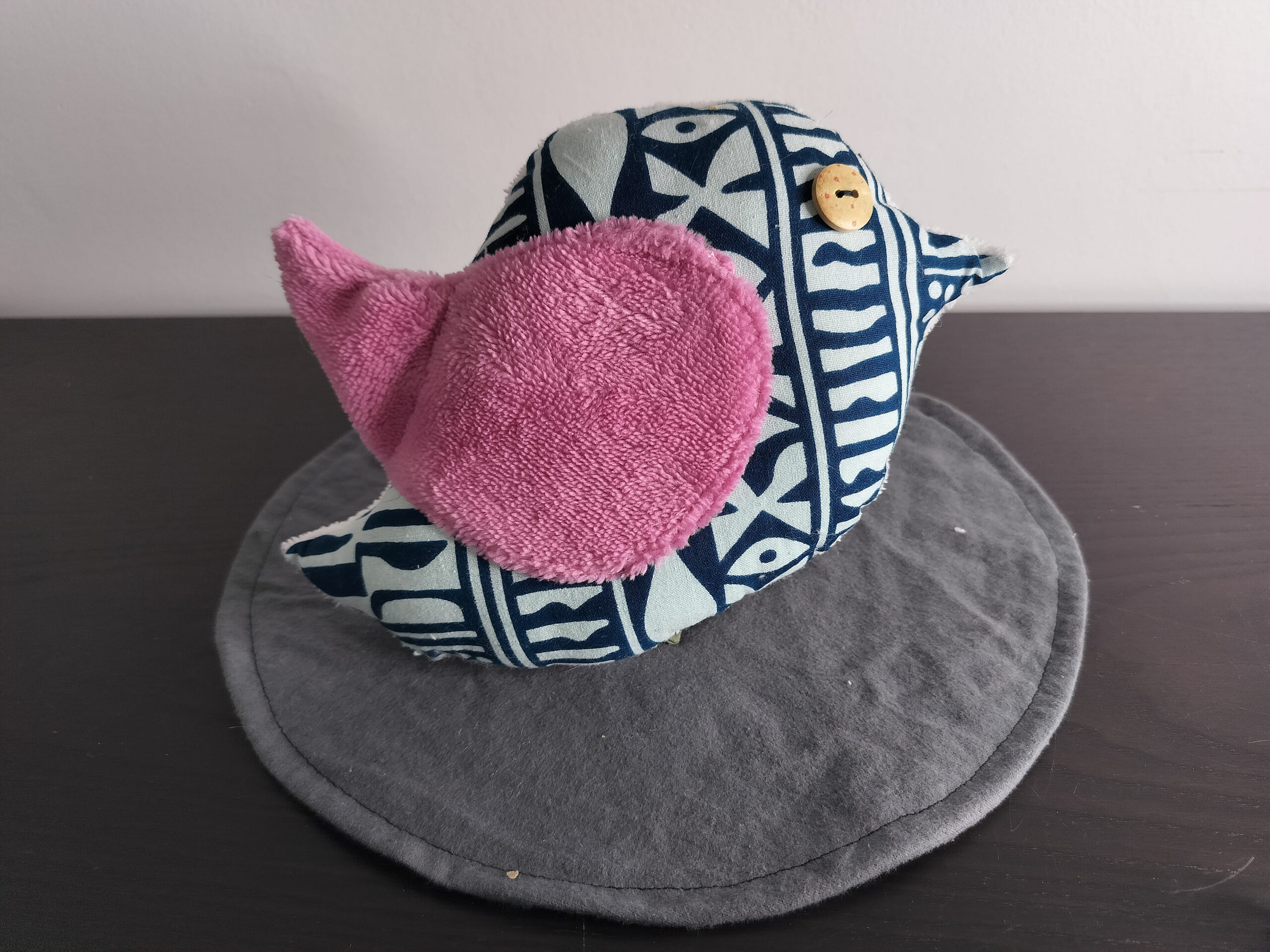 Oiseau décoratif en tissu wax bleu avec une aile en éponge rose et un œil bouton en bois.
