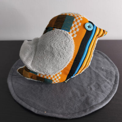 Peluche oiseau aux motifs géométriques avec une aile en éponge gris clair et un œil bouton bleu.