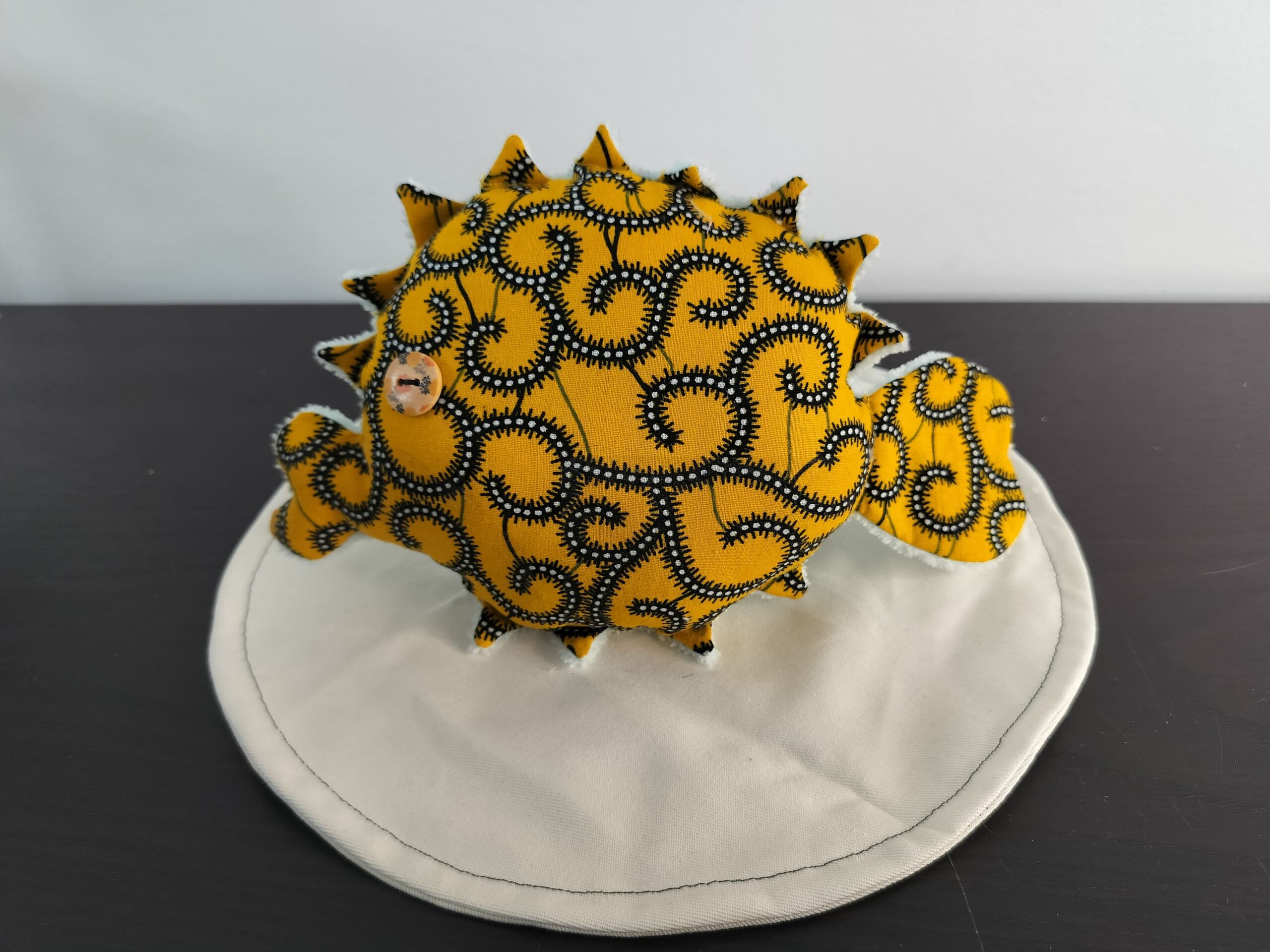 Peluche poisson globe Cameroun fait main en tissu jaune moutarde a motifs de volutes noires et blanches oeil bouton marron et texture peluche blanche