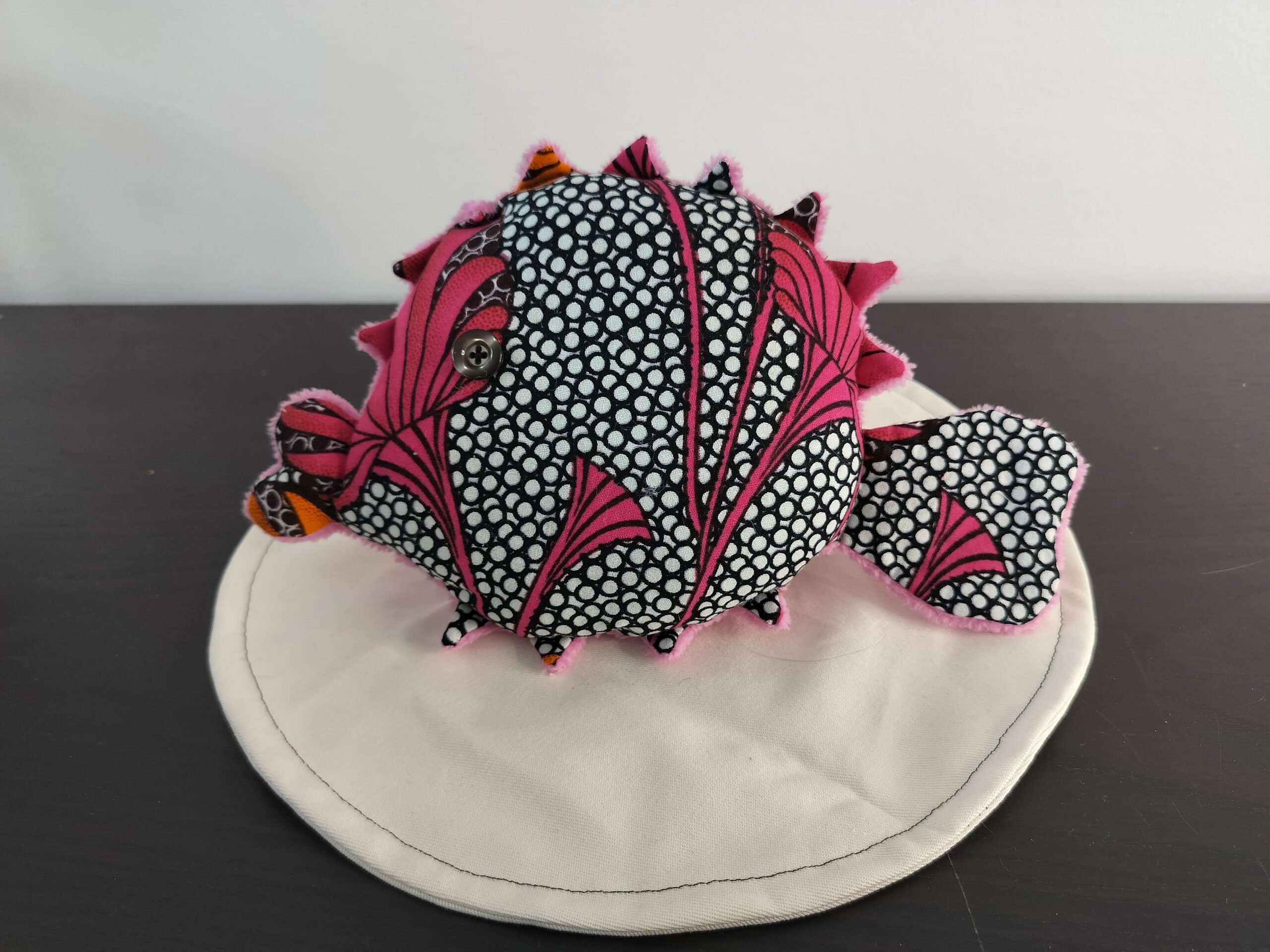Peluche poisson globe Cameroun fait main en tissu rose fuchsia a motifs de cercles noirs et blancs oeil bouton noir et pointes orange avec texture peluche rose