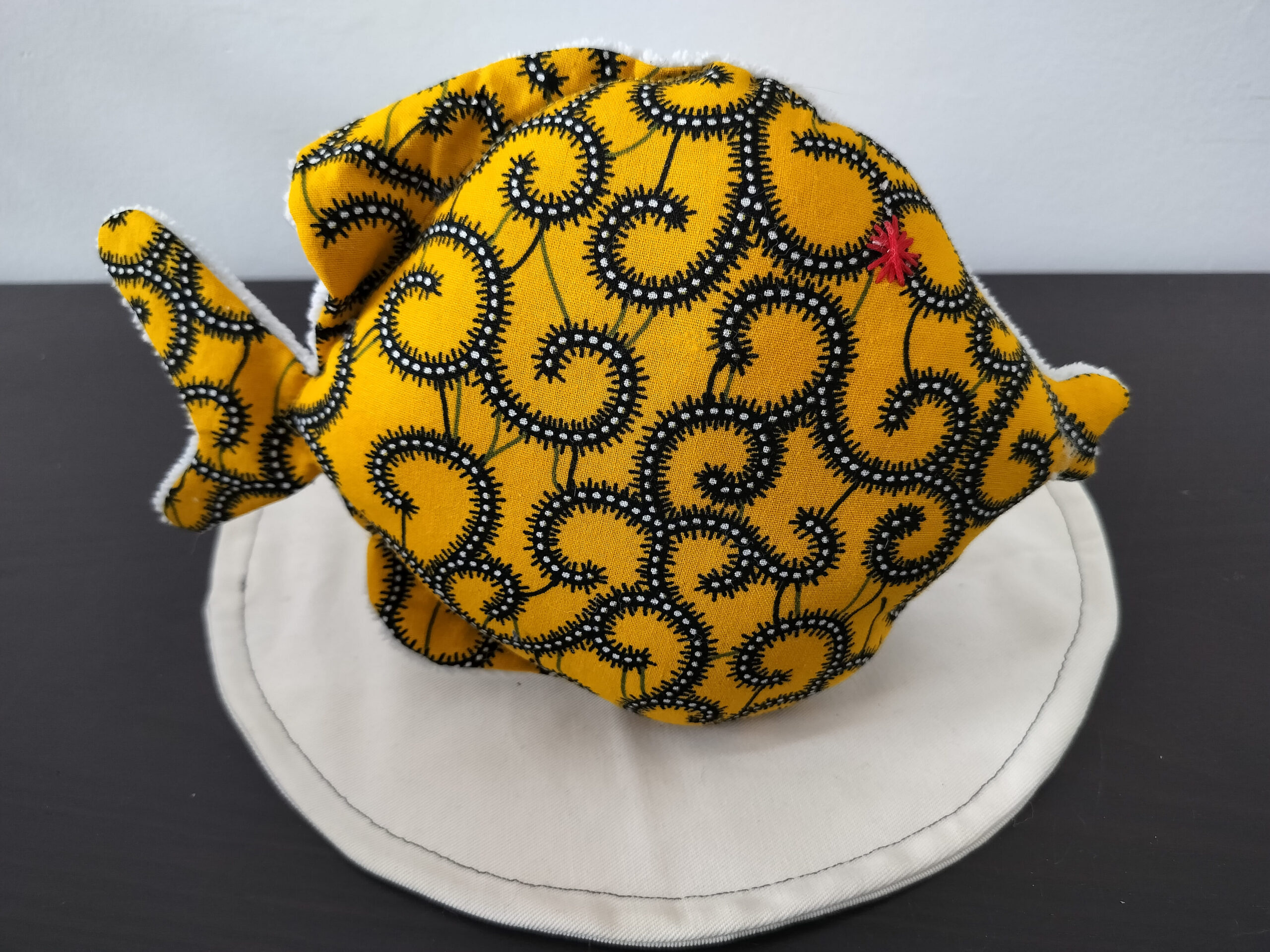 Peluche poisson rond de la collection Cameroun en tissu Wax jaune à motifs spirales avec un œil étoile rouge brodé main.