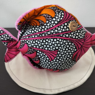 Peluche poisson rond de la collection Cameroun en tissu Wax rose et orange avec un œil bouton en bois gravé style horloge ancienne.