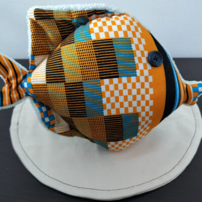 Peluche poisson rond de la collection Cameroun en tissu géométrique orange, noir et bleu avec un œil bouton noir classique.