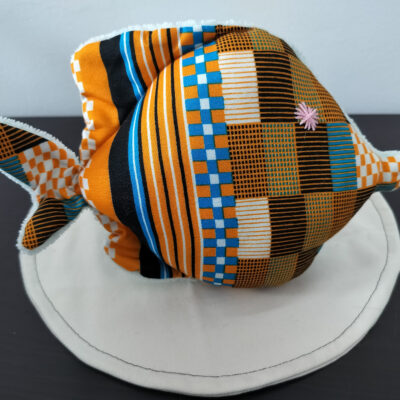 Peluche poisson rond de la collection Cameroun en tissu géométrique orange, noir et bleu avec un œil étoile rose brodé main.