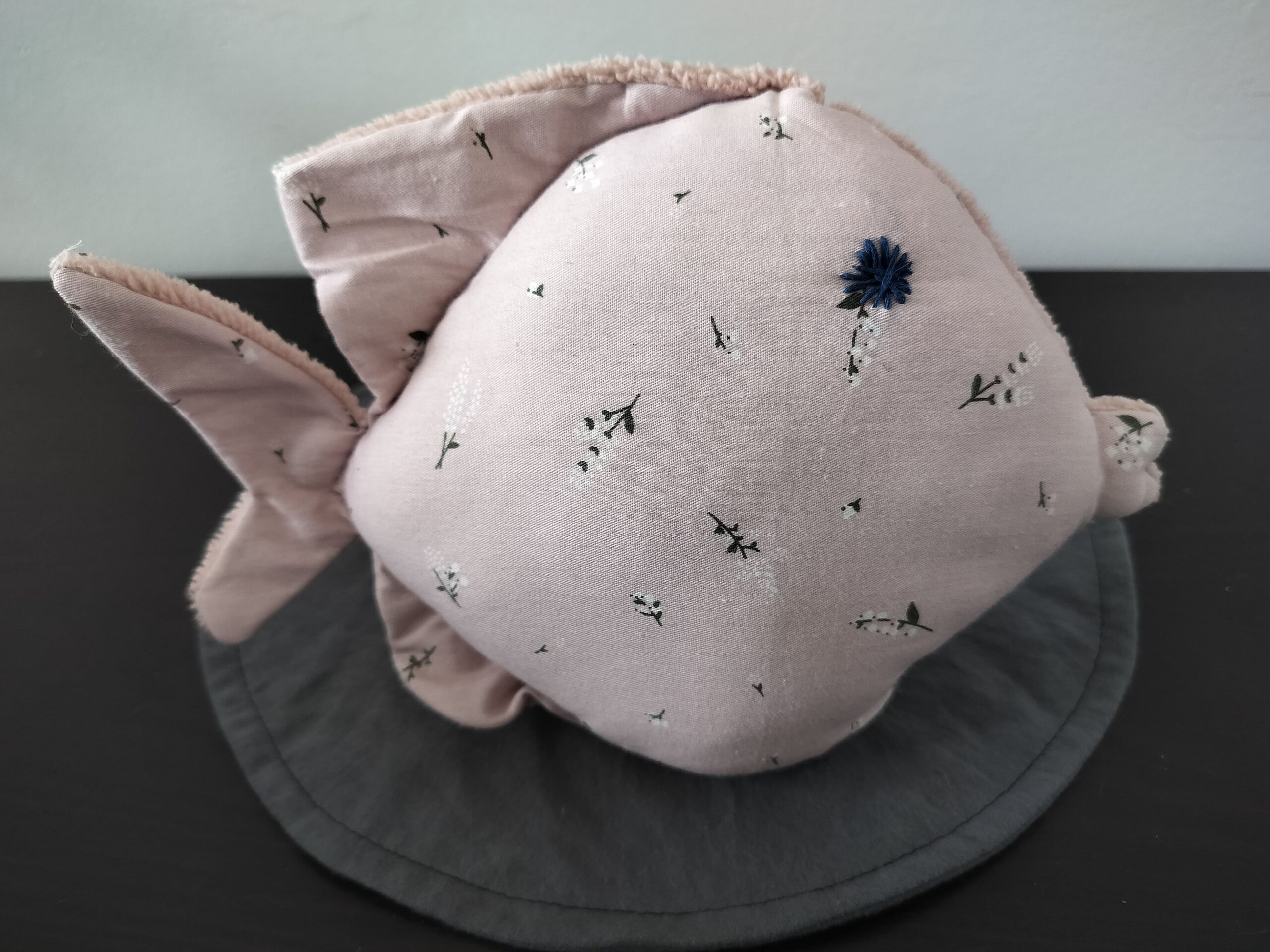 Peluche poisson rond au tissu vieux rose à motifs de brins de muguet avec un œil étoile bleu marine brodé main.
