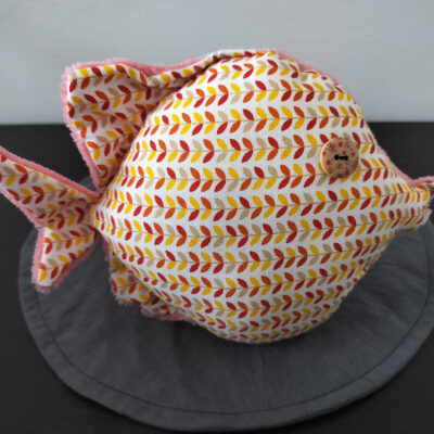 Peluche poisson rond au tissu blanc imprimé d'épis terracotta et jaune avec un œil bouton en bois moucheté.