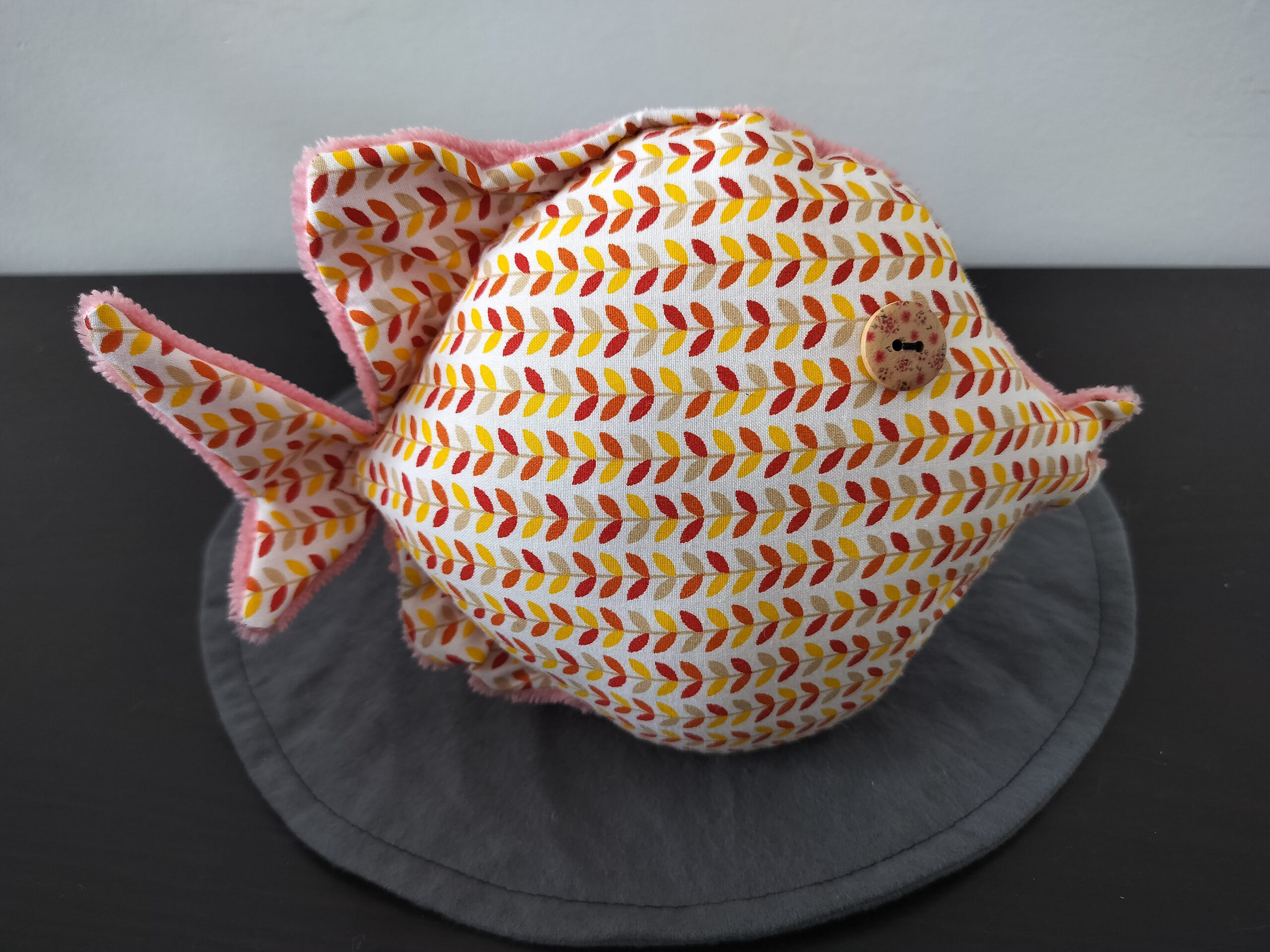 Peluche poisson rond au tissu blanc imprimé d'épis terracotta et jaune avec un œil bouton en bois moucheté.