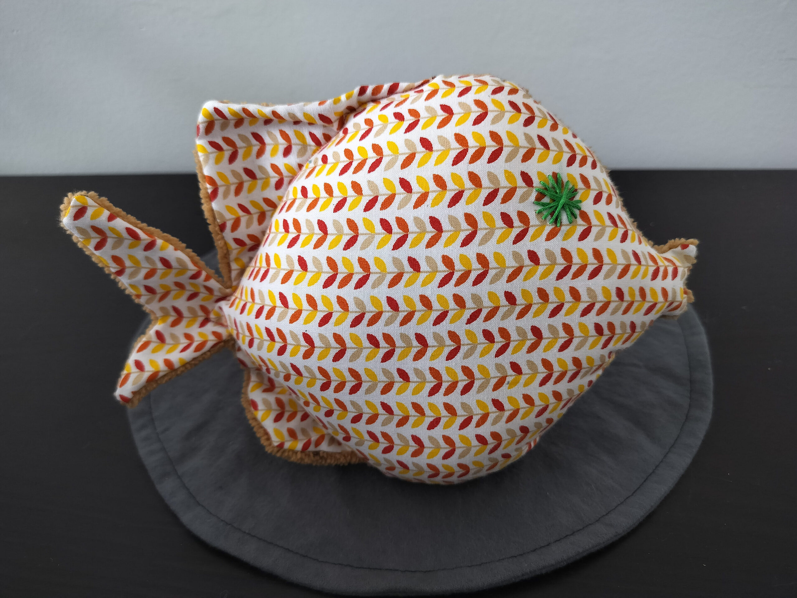 Peluche poisson rond au tissu blanc imprimé d'épis terracotta et jaune avec un œil en forme d'étoile vert sapin brodé main.
