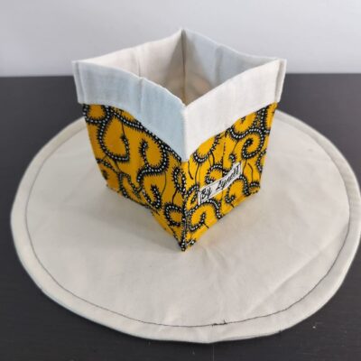 Vide-poche en tissu wax jaune et coloré, petit panier carré bicolore avec revers blanc un tissu au style wax jaune vibrant, mariant un fond jaune lumineux à des motifs tourbillonnants noirs et blancs.