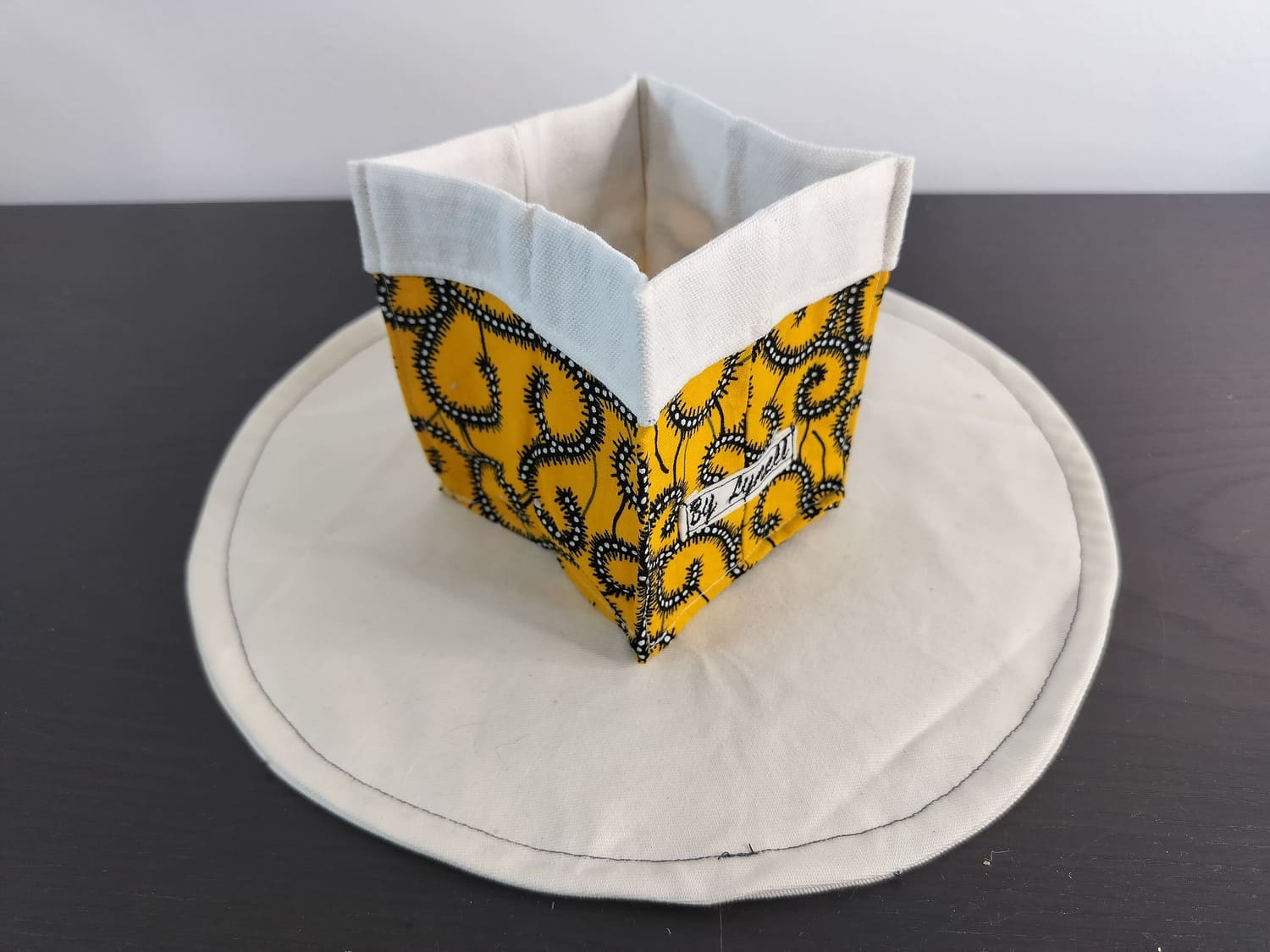 Vide-poche en tissu wax jaune et coloré, petit panier carré bicolore avec revers blanc un tissu au style wax jaune vibrant, mariant un fond jaune lumineux à des motifs tourbillonnants noirs et blancs.
