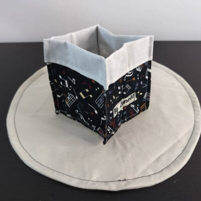 Vide-poche en tissu musical, petit panier carré bicolore avec revers blanc un coton au style musical et rythmé, mêlant un fond noir profond à des illustrations d'instruments et de portées musicales.